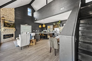 Un interno moderno con camino in pietra, pareti in legno scuro, una cucina con elettrodomestici in acciaio inossidabile e un’area pranzo con tavolo e sedie.