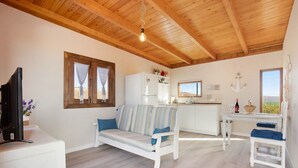 Una habitación con techo de madera, un sofá, una mesa de comedor, una zona de cocina y un televisor.