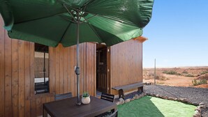 Una cabaña de madera con una mesa de comedor, sillas y un paraguas verde.