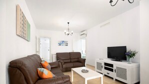 Ein Wohnzimmer mit braunem Sofa, einem weißen Couchtisch und einem Fernseher auf einem weißen Schrank.