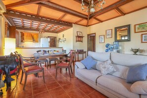 A spacious living area with a sofa, dining table, and chairs. A kitchen is visible in the background. - Rural Vacation Home "Los Miradores" with Private Pool, 2 Private Terraces & Wi-Fi (Marchena)