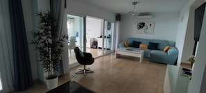 A living room with a sofa, a chair, a coffee table, a potted plant, and a sliding glass door leading to a balcony. - Vacation Home "Beach House El Saladillo" with Sea View, Private Tennis Court & Wi-Fi (Estepona, Saladillo Benamara)