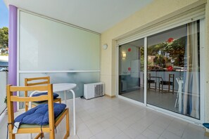 Une pièce comprenant une chaise en bois, une petite table et une porte-fenêtre coulissante donnant sur un espace extérieur aménagé avec des chaises et une table.