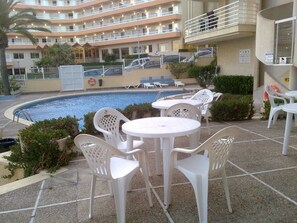 Un espace piscine d’hôtel comprenant plusieurs chaises longues et tables, une piscine et, en arrière-plan, un immeuble à plusieurs étages.