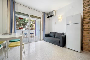 A room with a dining table, chairs, a sofa, a refrigerator, and an air conditioning unit. - Holiday Apartment "Font De Mar" with Sea View, Private Terrace & Shared Pool (Salou)