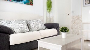 A living room with a sofa, a coffee table, a potted plant, a painting, and a door. - Holiday Home "Casa Centro Historico Barbate" with Private Terrace and Wi-Fi (Barbate)