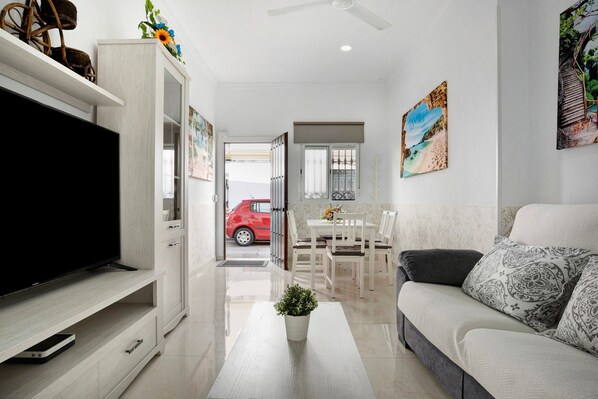 A modern living room with a flat-screen TV, a sofa, a dining area, and artwork on the walls.