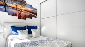 A bedroom with a bed, white walls, and a cityscape painting. - Holiday Home "Casa Centro Historico Barbate" with Private Terrace and Wi-Fi (Barbate)