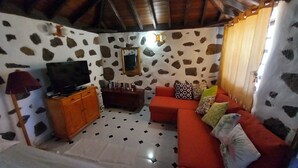 A room with a stone-patterned wall, a television on a wooden cabinet, a red sofa with patterned cushions, and a tiled floor. - Holiday Home 'La Carpintera' with Sea View, Private Terrace and Wi-Fi (Tijarafe)