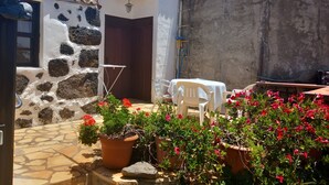 A courtyard with a stone wall, a door, a small table with chairs, and potted plants with red flowers. - Holiday Home 'La Carpintera' with Sea View, Private Terrace and Wi-Fi (Tijarafe)