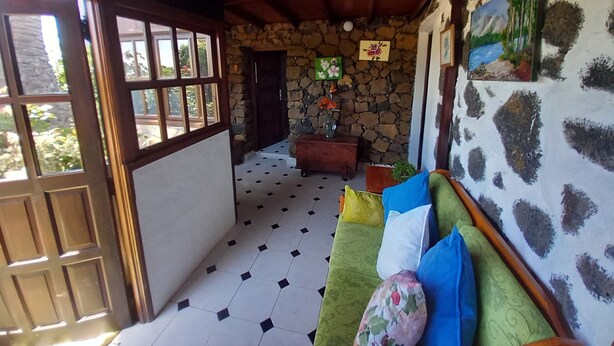 A room with a stone wall, a green sofa with multiple cushions, a wooden ceiling, and a tiled floor. - Holiday Home 'La Carpintera' with Sea View, Private Terrace and Wi-Fi (Tijarafe)