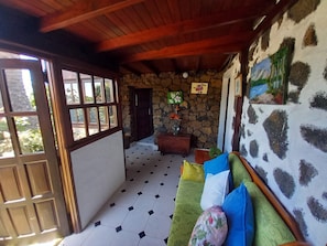 Ein Zimmer mit einer Steinsäule, einem grünen Sofa mit vielen Kissen, einer Holzzielung und einem Fliesenboden.