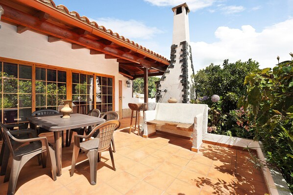 A patio with a table and chairs, a stone bench, and a chimney.