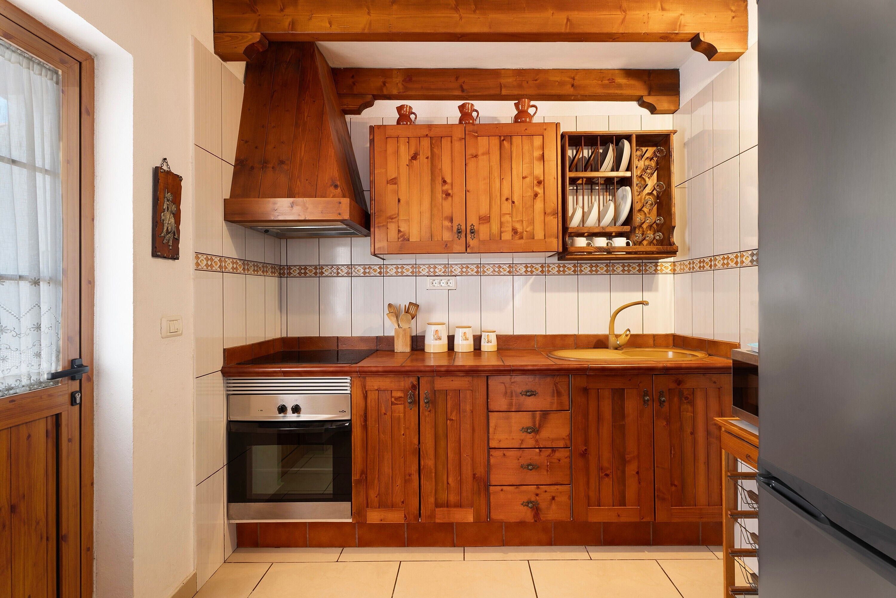 Een keuken met houten kastjes, een fornuis, een spoelbak en een houten plank boven de spoelbak.