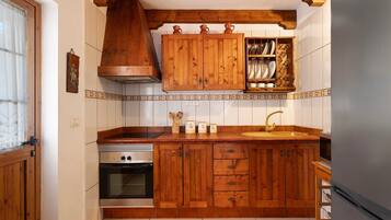 Een keuken met houten kastjes, een fornuis, een spoelbak en een houten plank boven de spoelbak.