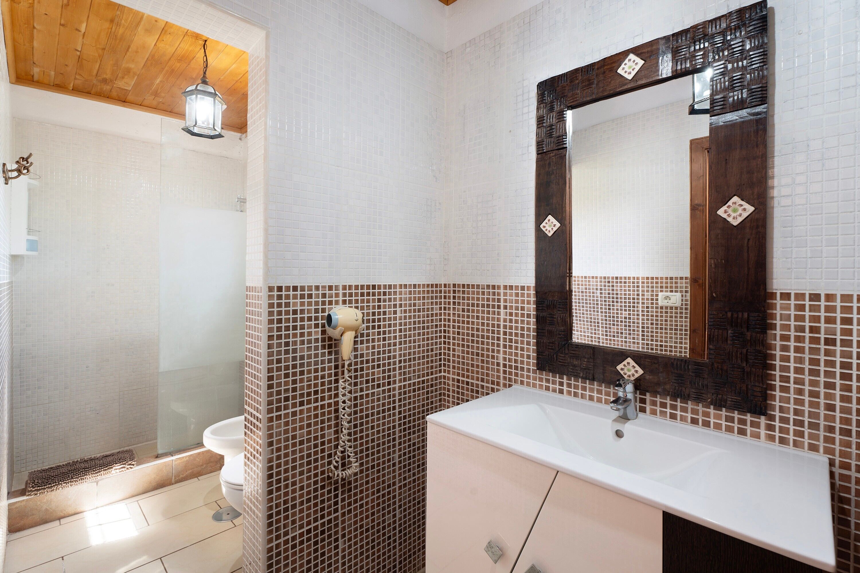 Een badkamer met douche, toilet, wastafel en een spiegel met decoratieve lijst.