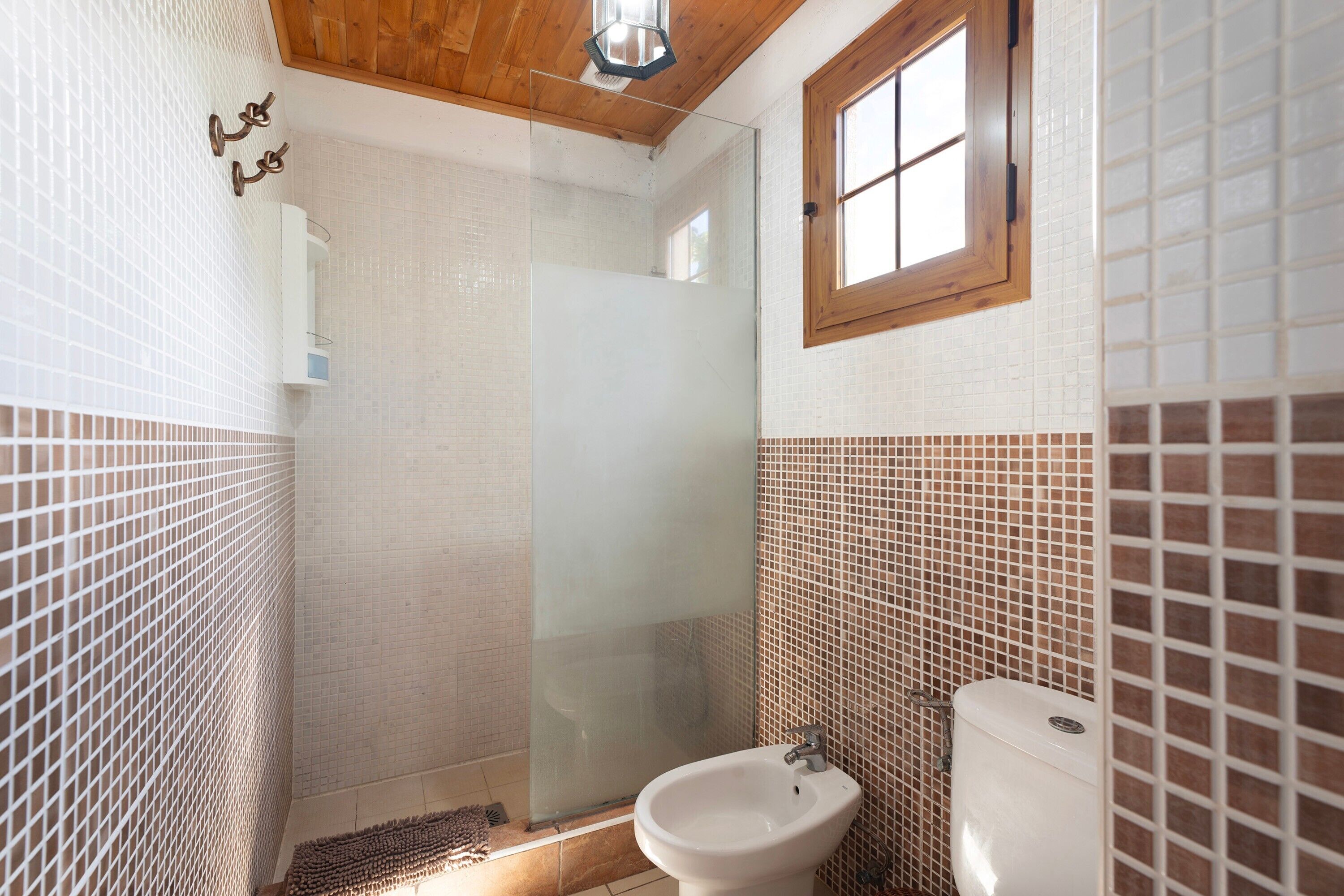 Een badkamer met een douchecabine van glas, een witte bidet en een raam met houten kader.