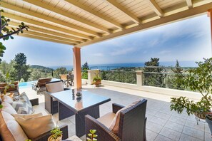 A covered outdoor seating area with wicker furniture, a pool, and a view of the sea.
