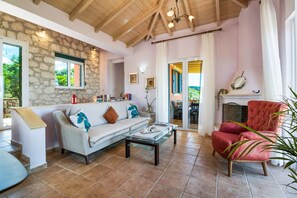 A cozy living room with a stone wall, a sofa, a red armchair, and a fireplace. - Villa 'Belvedere Rosa' with Sea View, Pool, Terrace & Wi-Fi (Lefkada)