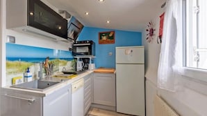 A compact kitchen with a microwave, stove, and refrigerator, a blue wall with a painting, and a window with curtains. - Guest House 'Domaine De Pharaon' with Shared Terrace, Wi-Fi and Air Conditioning (Morlaix)