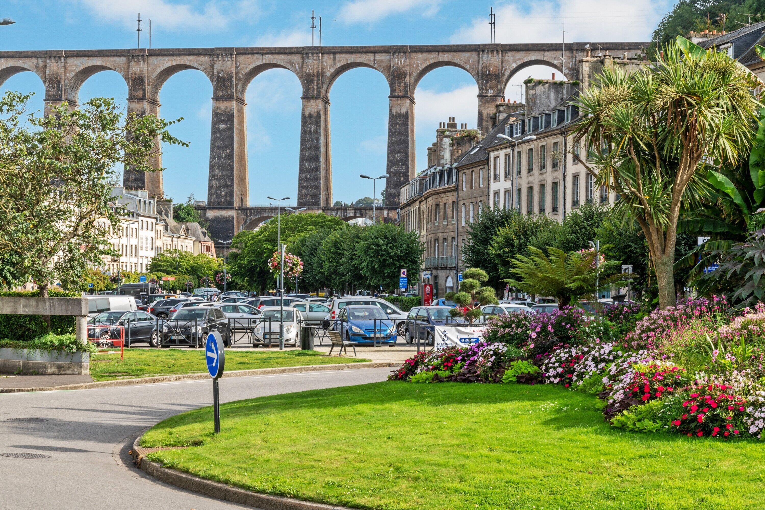 A street with a large bridge, parked cars, and a grassy area with flowers.