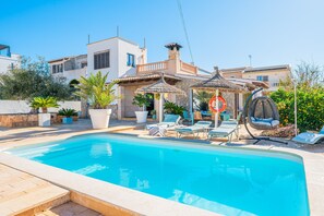 En swimmingpool med liggestole, en pergola og en stenvæg.