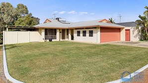 Une maison de plain-pied avec un garage rouge, une véranda et un jardin clôturé.