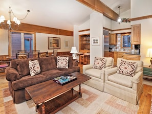 A cozy living room with a brown sofa and a beige armchair, both with patterned cushions. There's a wooden coffee table in front of the sofa. - All Seasons | 4BR Condo Steps to Vail Village, Sleeps 12 (Vail)