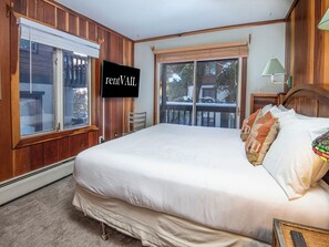 A bedroom with a large bed, a television mounted on the wall, and a view of the outside through the windows.