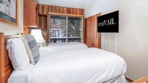 Una camera d'albergo con un letto grande, una televisione montata a parete e una finestra con persiane.