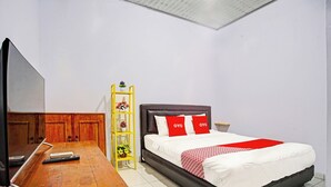 Un dormitorio con cama, un escritorio de madera, un televisor y una estantería amarilla con plantas.