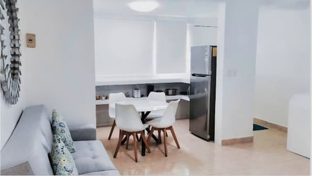 A modern kitchen with white cabinets, a dining table with four chairs, and a refrigerator. - Departamentos Villas Capdeviel (Cancun)