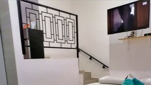 A staircase with a geometric railing design, a flat-screen TV mounted on the wall, and a white sofa with teal cushions. - Departamentos Villas Capdeviel (Cancun)