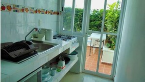 A kitchen with a gas stove, sink, and a window overlooking a garden. - Departamentos Villas Capdeviel (Cancun)