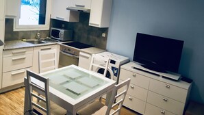 Een kleine keuken met witte kastjes, een magnetron, een fornuis, een spoelbak en een televisie op een dressoir.
