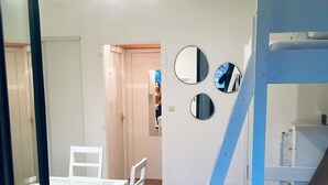 Een kamer met een stapelbed, een eettafel met stoelen en een spiegel aan de muur.