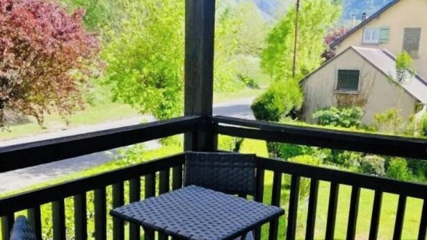 Een overdekt balkon met twee opklapbare stoelen en een tafel, met uitzicht op een groen landschap met bomen en een berg in de verte.