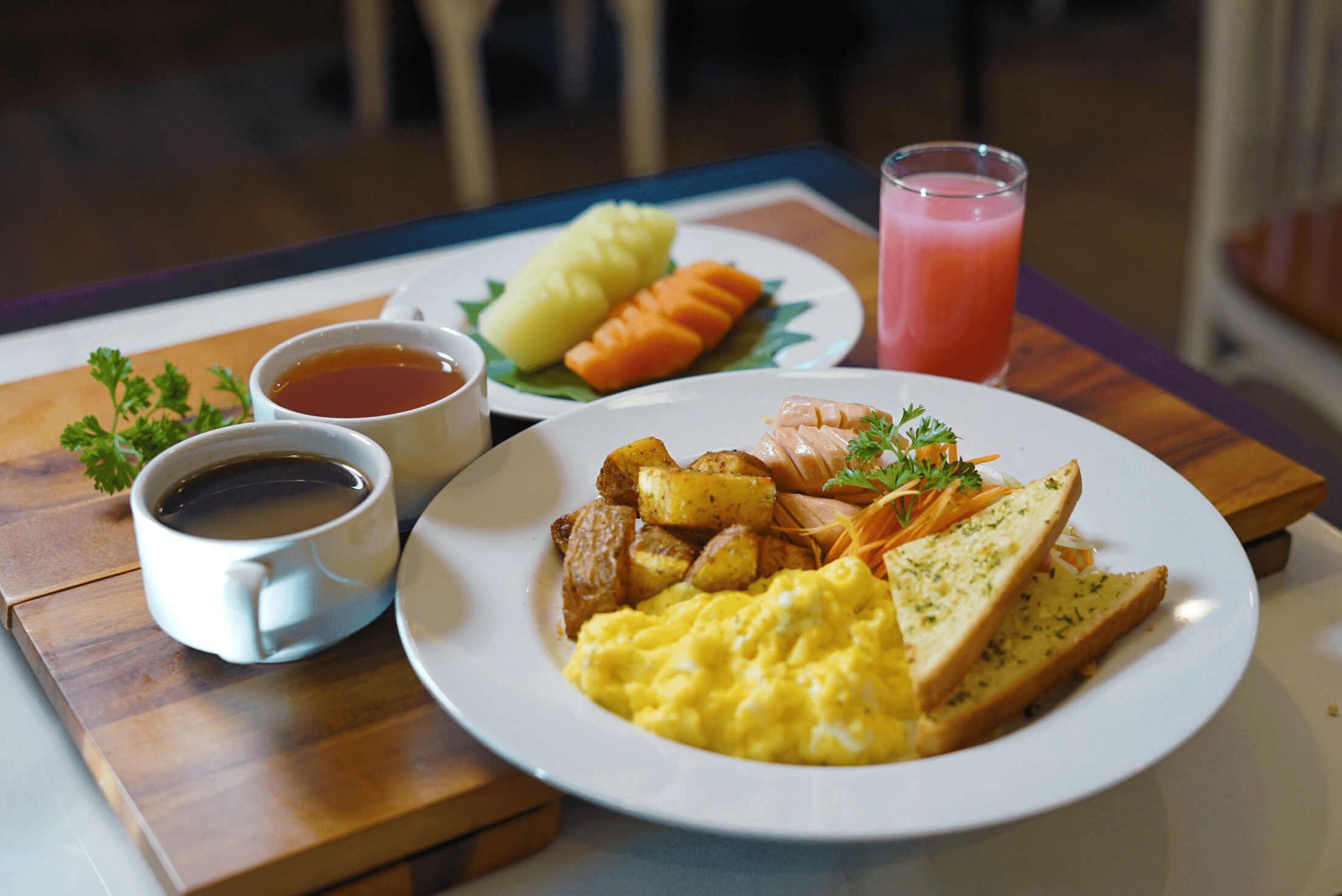 A breakfast plate with scrambled eggs, toast, potatoes, carrots, and salmon, accompanied by a cup of coffee and a glass of juice.