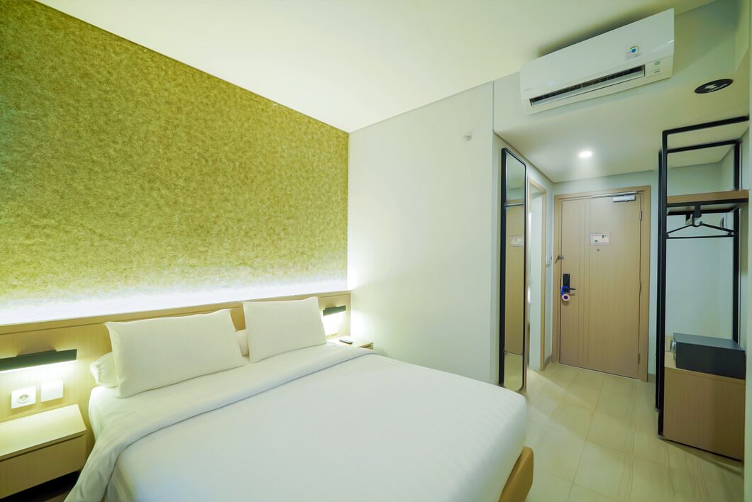 A hotel room with a bed, bedside tables, an air conditioning unit, a wardrobe, and a mirror.