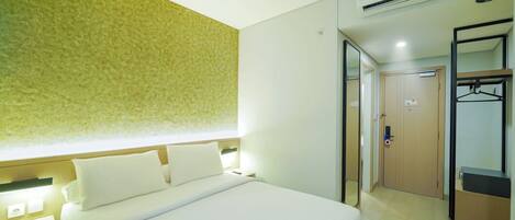A hotel room with a bed, bedside tables, an air conditioning unit, a wardrobe, and a mirror.