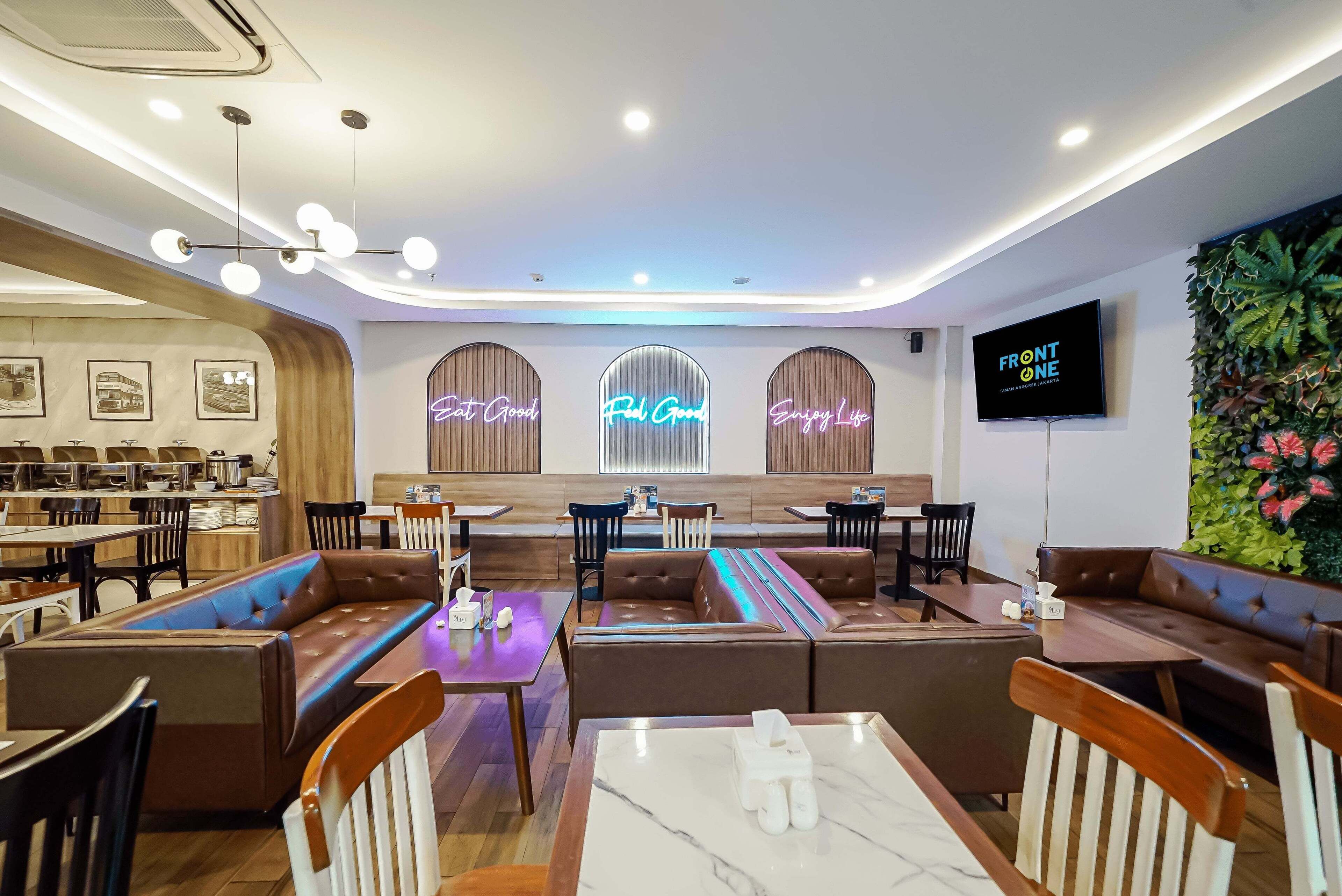 Een modern restaurant met zitplaatsen in cabines en aan tafels, neonborden, een televisie en een groene wand.