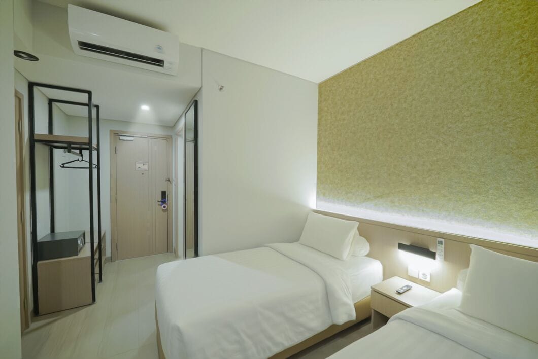 Habitación de hotel con dos camas, un armario, un espejo y una mesita de noche con lámpara.