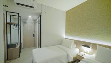 Ein Hotelzimmer mit zwei Betten, einem Kleiderschrank, einem Spiegel und einem Nachttisch mit Lampe.