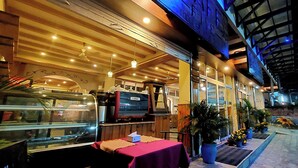 En restaurang utomhus med träbord och stolar, en disk där maten visas upp och krukväxter.
