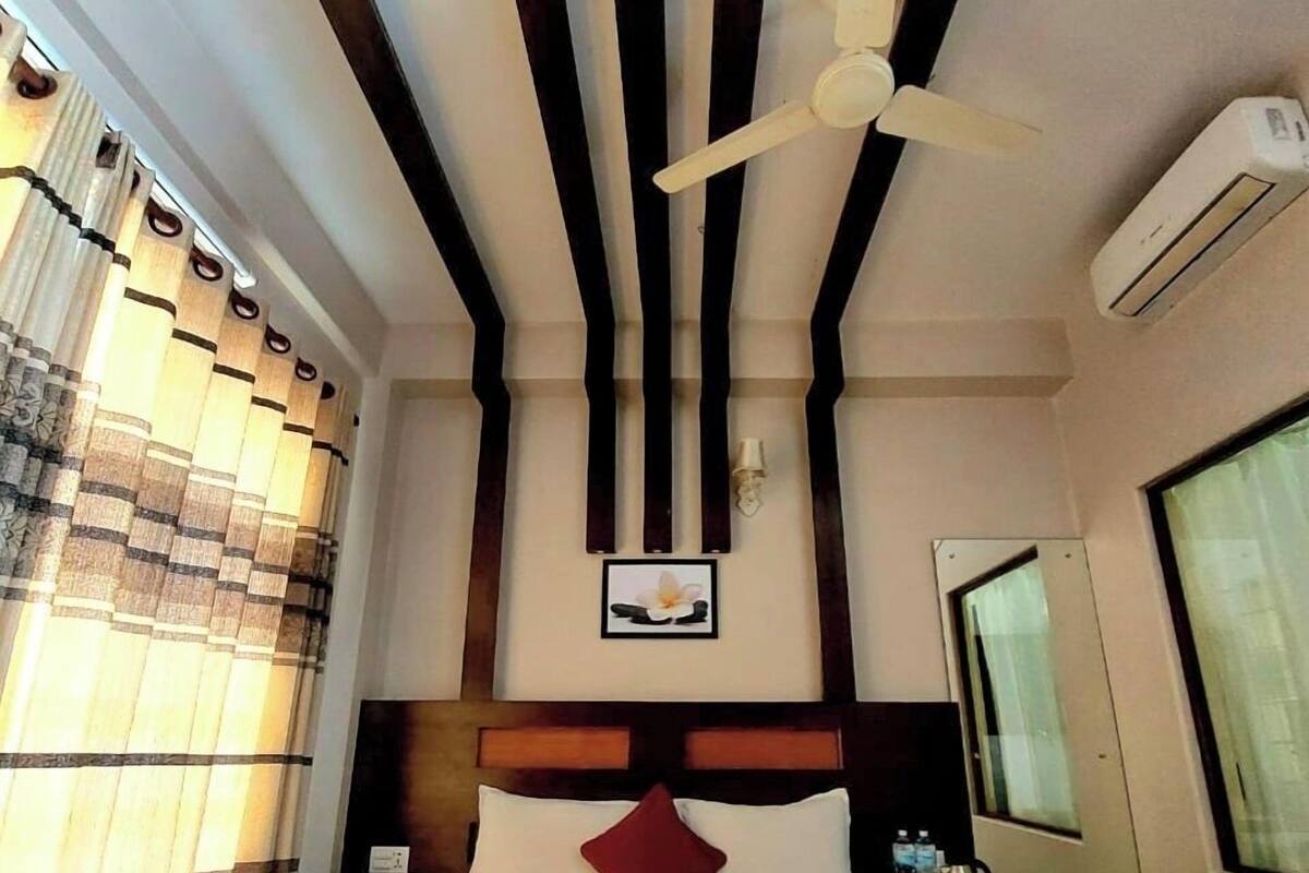 Ein Hotelzimmer mit einem Bett, einem Deckenventilator, einer Klimaanlage und einem mit Vorhängen versehenen Fenster.