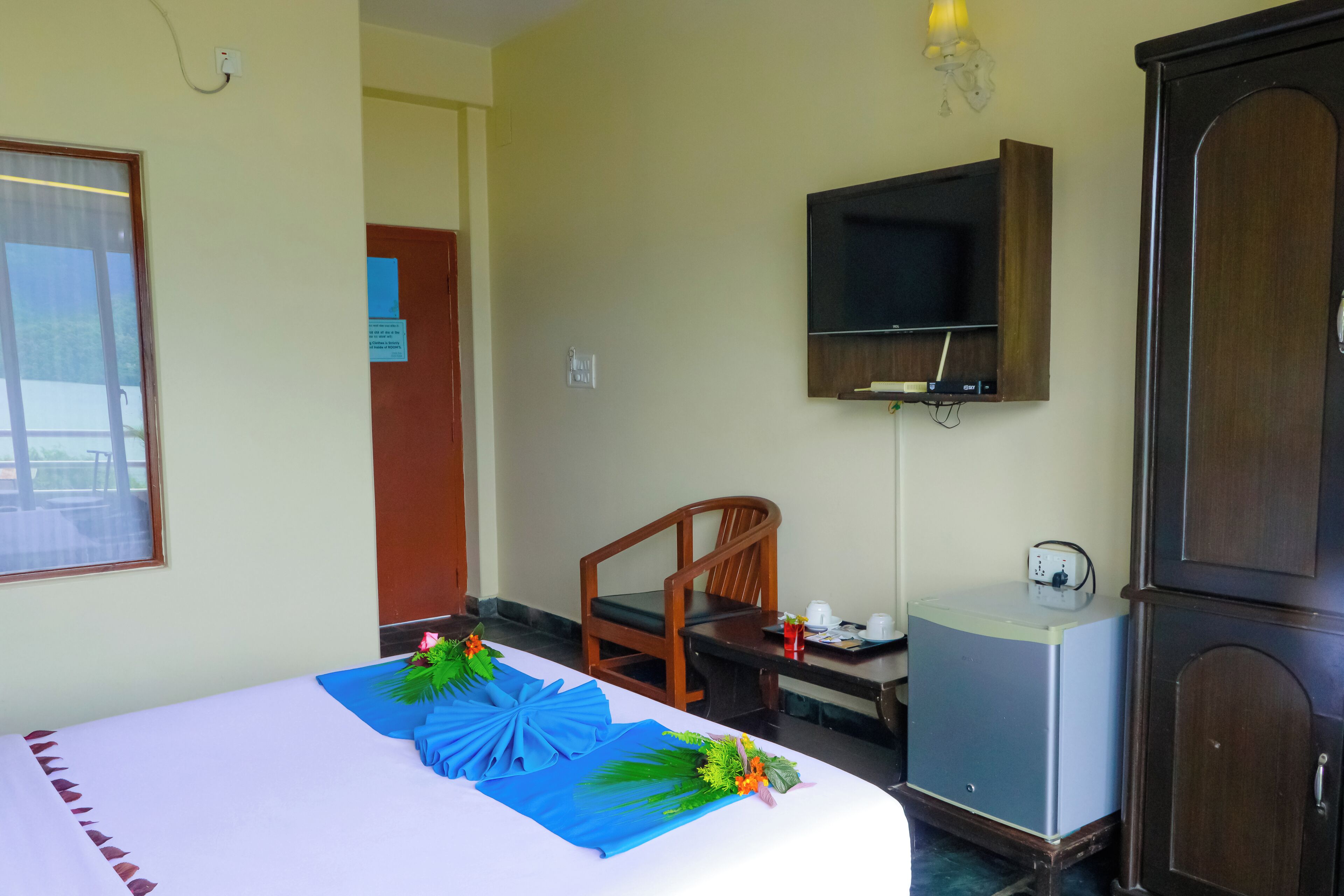 Una habitación de hotel con cama, escritorio, silla, televisor y un pequeño armario.