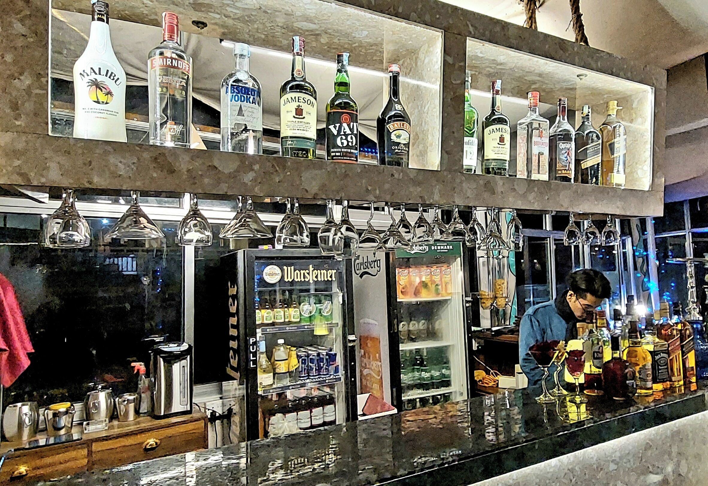 A bar area with shelves of liquor bottles and a minibar stocked with beverages.