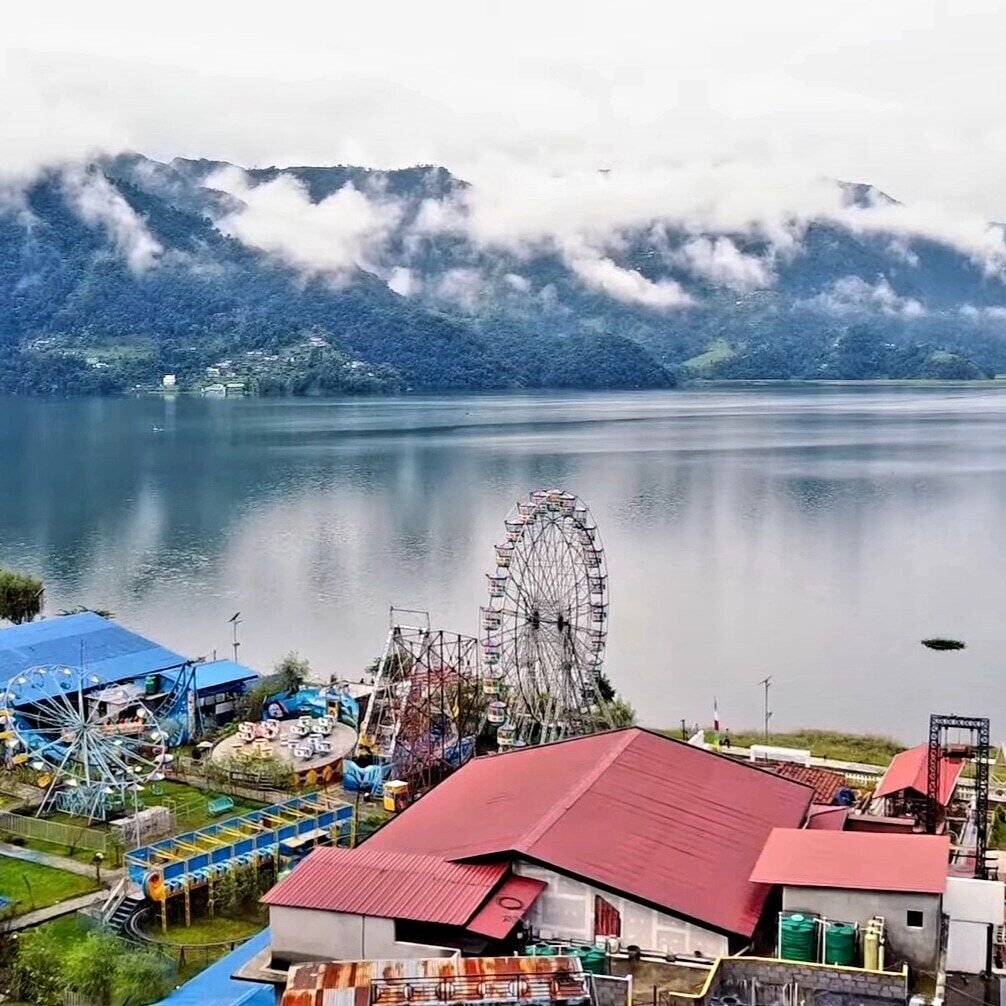 A lakeside amusement park with a Ferris wheel, roller coaster, and various rides.