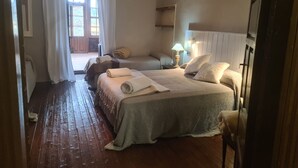 Een hotelkamer met twee bedden, een houten vloer, een lamp en uitzicht op buiten.