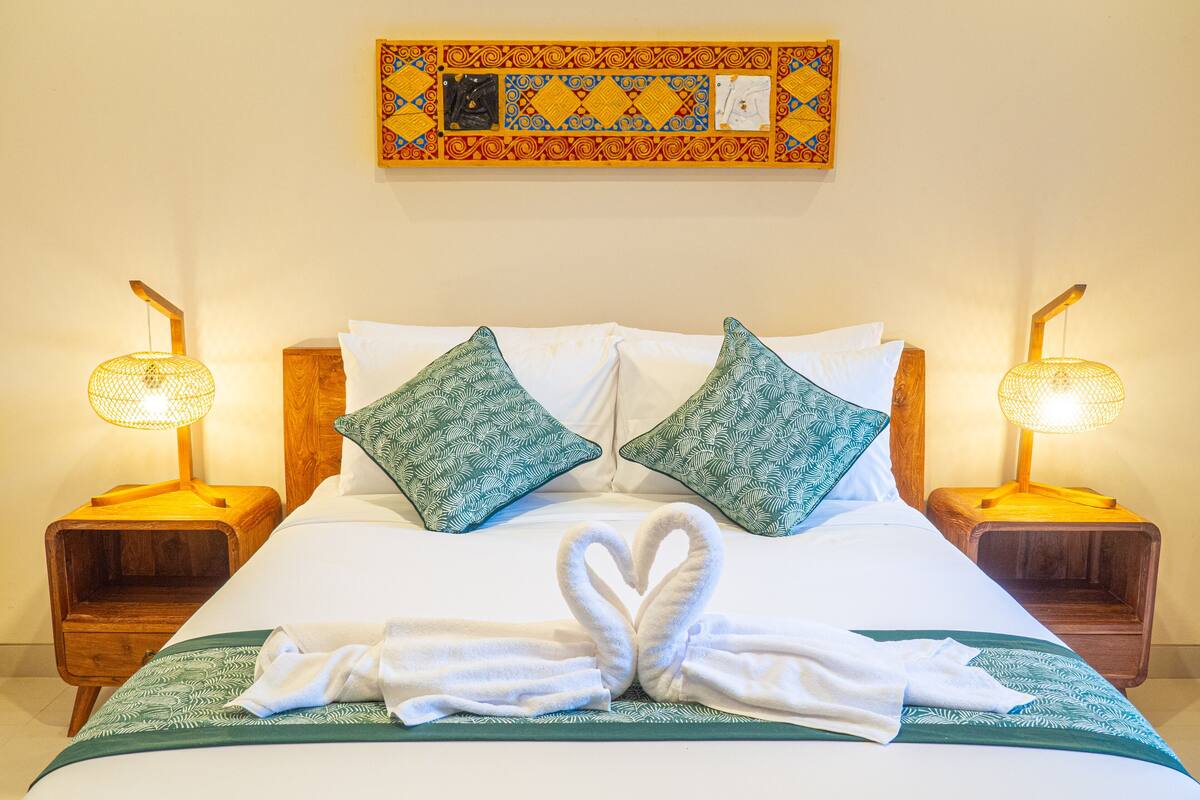 A neatly made bed with two pillows, a heart-shaped towel arrangement, and two bedside lamps.